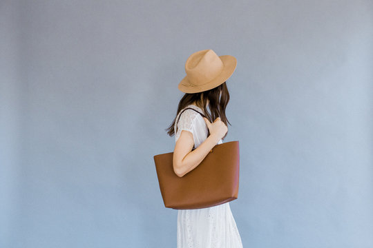 Fashionable woman holding bag against backdrop
