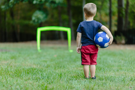Young boy looking towards a practice goal with a soccer ball under his arm