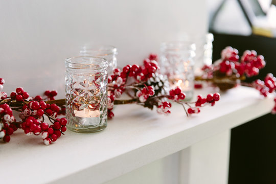 Red berry Christmas garland and votives on a mantlepiece.