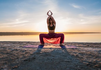 woman on the beach at sunset starts doing yoga asana training . Morning natural stretch warm-up training