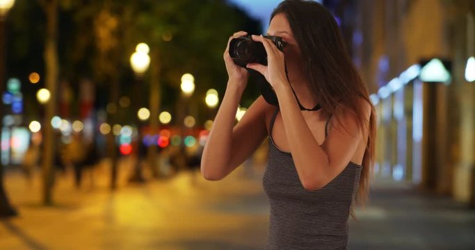 Pretty tourist woman taking picture with dslr camera on the Champs-Elysees, Traveling girl wearing striped tank top taking photo in Paris, France at night, 4k