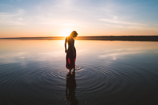 Silhouette woman on the beach at sunset . She stands in water. Morning natural stretch warm-up training