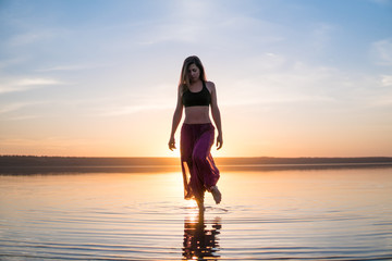 Silhouette woman on the beach at sunset standing in water. Morning natural stretch warm-up training