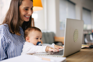 Young mother taking care her baby while working at home.