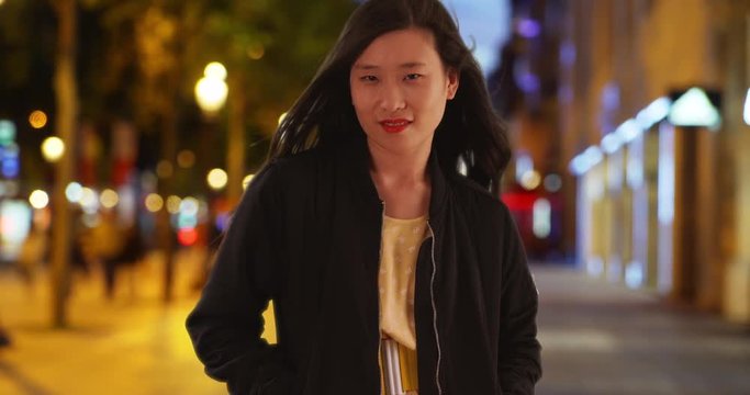 Chinese woman wearing black bomber jacket standing on city street at night, Asian millennial female with hands in pockets, 4k
