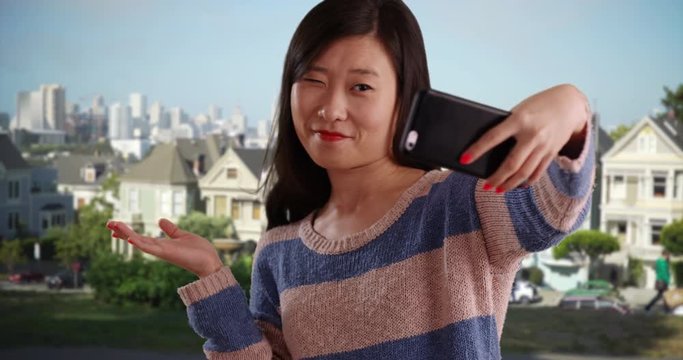 Casual millennial woman using smartphone to take selfie in front of Painted Ladies San Francisco, Close up of happy young Asian women taking selfie with cell phone camera by California landmark, 4k
