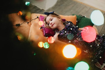 Little lovely girl laying on the floor on pillows among the colorful lights