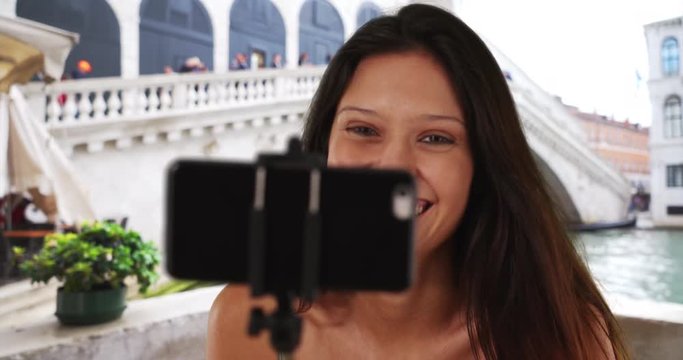 Cute traveler woman taking phone selfie in Venice, Italy near famous bridge on the Grand Canal, Close up of sexy Caucasian girl enjoying summer vacation taking photos by Rialto Bridge, 4k