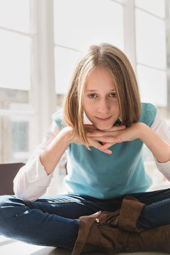 tween girl sitting cross-legged on table, looking at camera