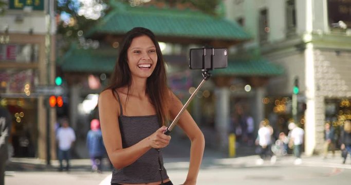 Cute traveler girl taking photos with selfie stick in Chinatown, San Francisco, Trendy young tourist woman in striped tank top taking selfies with smartphone, 4k