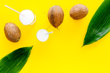 Light cocktail with coconut milk. White tropical beverage in glasses with straw on yellow background with coconut and palm leaves top view space for text