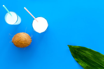 Light cocktail with coconut milk. White tropical beverage in glasses with straw on blue background with coconut and palm leaves top view copy space
