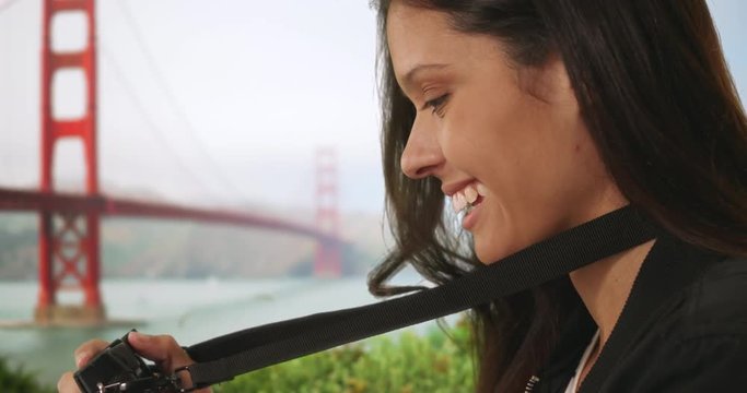 Side view of tourist woman in bomber jacket taking photo with dslr camera near Golden Gate Bridge, Millennial female focuses camera lens and takes snapshot while traveling in San Francisco, 4k