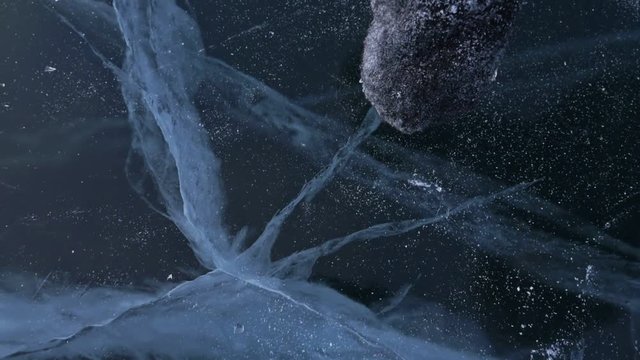 Men in the mittens twists the ice on the ice. Slow motion. The camera moves behind the ice. A piece of icy is very beautifully spinning on ice with magical cracks.