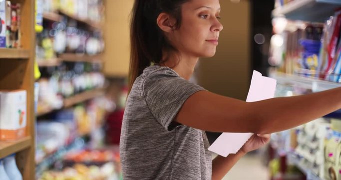 Close up of female customer in grocery store browsing shelf for item, Young woman reading from shopping list and choosing food, 4k