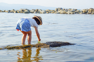A girl who plays with water at the sea. A girl who grabs something on the beach....