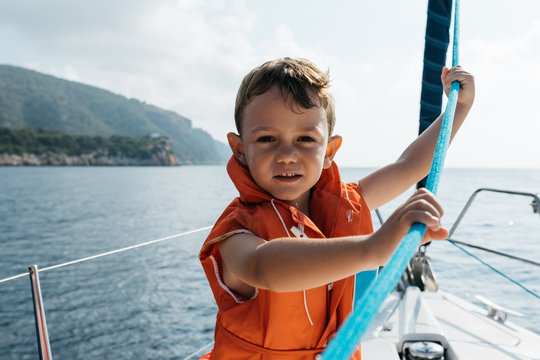 Smiling boy in life vest with rope in hands on yacht.