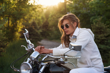 Fototapeta na wymiar Biker wearing sunglasses and jacket at wheel of a motorcycle. Guy with long hair and an earring. Stop on road trip.