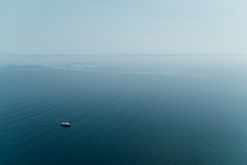 Lonely small fishing boat floating on shallow tranquil ocean water at dusk