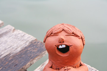 Laughing clay pottery dolls sitting on wood near river background