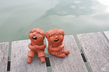 Laughing clay pottery dolls sitting on wood near river background