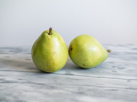 Two green pears on white marble countertop.