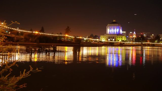 Oakland, California - June, 2016 - Wide shot timelapse of the Oakland Public Library and Lake Merritt lit up in Warriors colors at night.