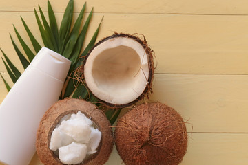 Coconut oil. Natural pure coconut oil and fresh coconuts in a section on a palm leaf on a yellow wooden plank background. cosmetics with coconut extract. Organic Natural Cosmetics 