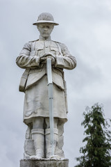 Naklejka premium Fort William, Scotland - June 11, 2012: Closeup of white stone war memorial statue on The Parade against gray sky. Shows young soldier in kilt contemplating.