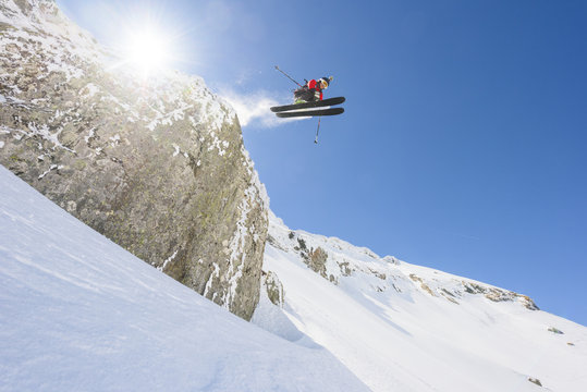 Male skier performing midair tricks jumping off snow-capped clif