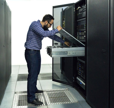 Technician performing maintenance tasks in a server room rack