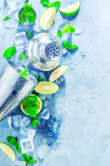 Shaker and bar accessories flat lay. Fresh mojito cocktail ingredients, mint, lime and ice cubes on a gray stone background. Summer drink concept with copy space.