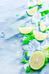 Mojito cocktail ingredients, mint, lime and ice cubes on a gray stone background with copy space. Making summer drinks close-up. Sunlight and refreshment concept.