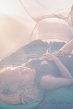 Young caucasian woman sleeping in translucent tent on the beach