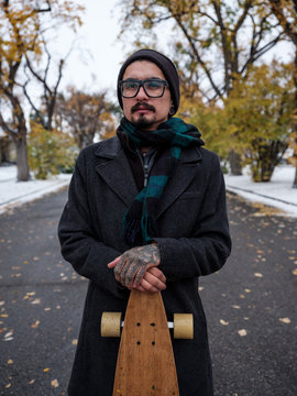 A longboarder poses in the middle of a street on a snowy autumn day