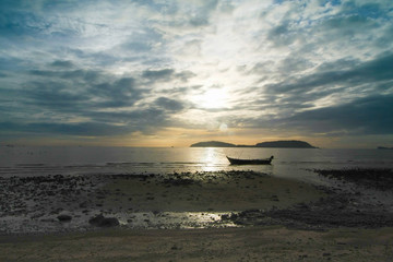 Boat float in the sea near beach in early morning and the Sun is growing up which has overlay clouds, dim light image..