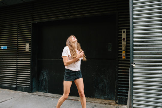 An attractive young woman wearing shorts and T-shirt laughing and looking up