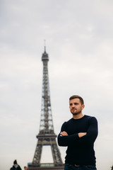 Fototapeta na wymiar Handsome man wearing a dark blue pullover is standing on the background of the Eiffel Tower