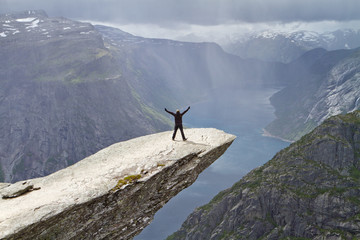 Man staying on Trolltunga rock (Troll's Tongue rock) and looking at Norwegian mountain landscape