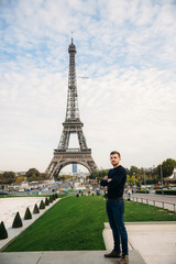 Handsome man wearing a dark blue pullover is standing on the background of the Eiffel Tower
