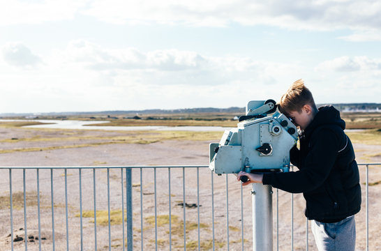 Teenage boy looking through a telescope on top of a building.