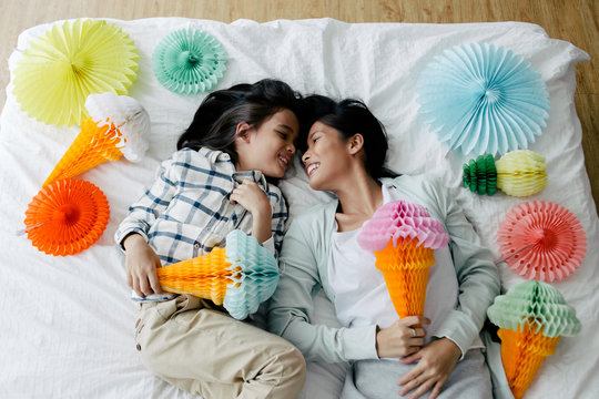 Asian mother and kid having fun playing with ice-cream cone shaped tissue paper lantern decoration in the bedroom
