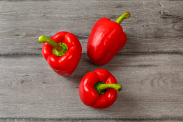 Table top view - three red bell peppers on gray wood desk.