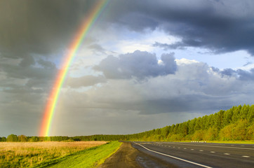 Naklejka na ściany i meble wet highway after rain with a rainbow against the backdrop of a rainy sky