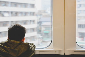 back side of little boy traveling by train and looking out through glass window, child problem or travel concept, vintage effect