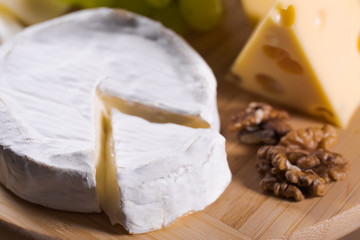 Different kinds of cheese on a plate with grapes and nuts