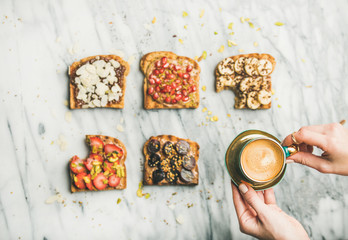 Healthy breakfast. Flat-lay of vegan wholegrain toasts with fruit, seeds, nuts, peanut butter and woman's hands with cup of coffee over light marble background, top view. Clean eating food concept