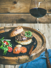 Pulled pork meat burger with vegetables and glass of red wine, wooden wall background, copy space © sonyakamoz