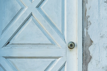 Silver knob on old white wooden door with concrete wall.