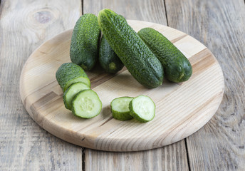 Several whole fresh cucumber and slices of cucumber on a cutting